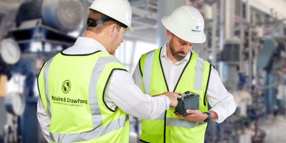 Two men wearing hard hats and yellow vests looking at a piece of instrumentation equipment