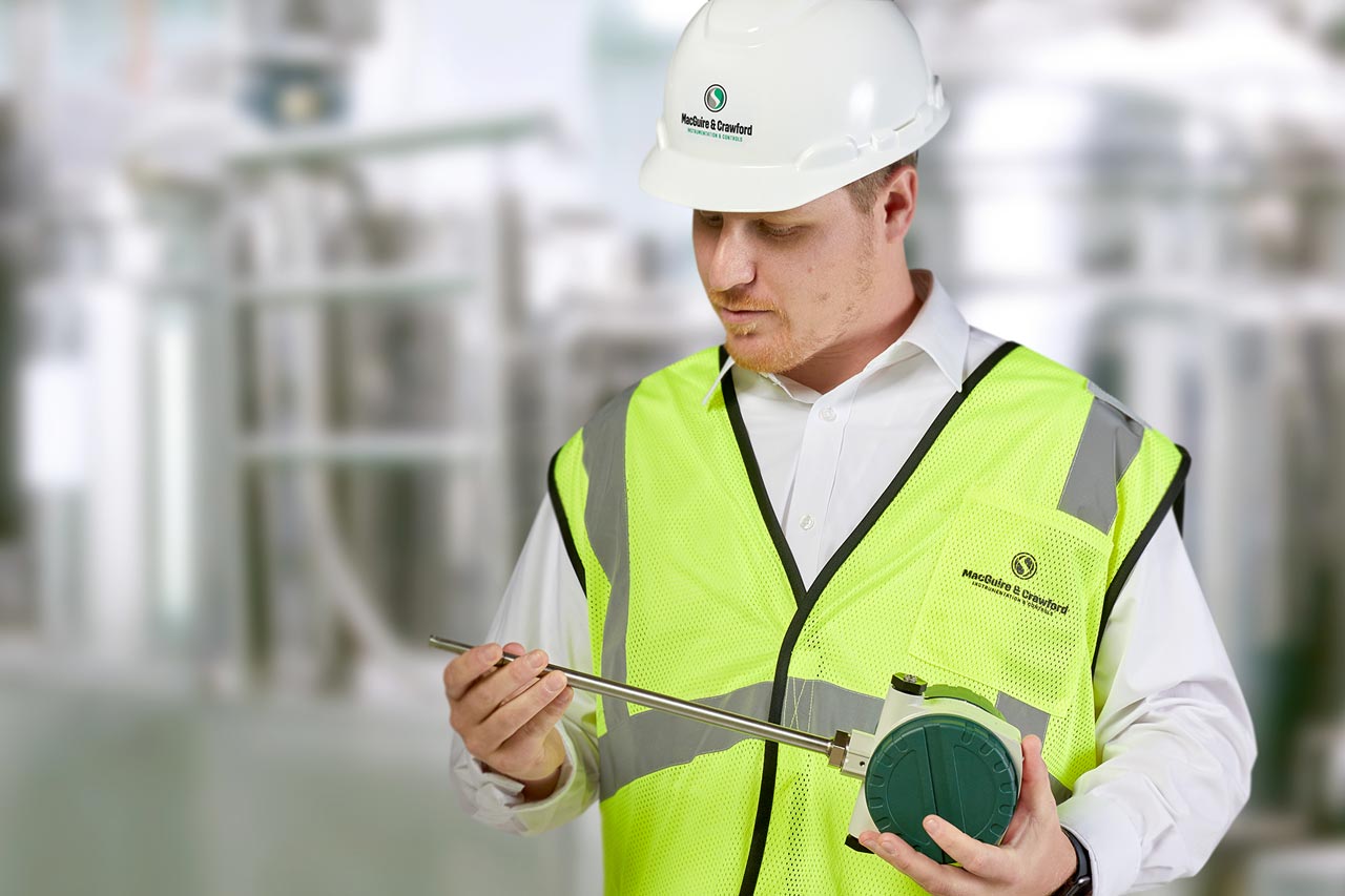 Man in a processing plant wearing a hard hat holding a measurement instrument