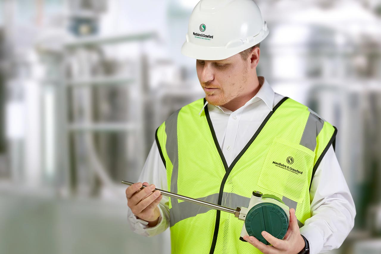 Man in a processing plant wearing a hard hat holding a measurement instrument