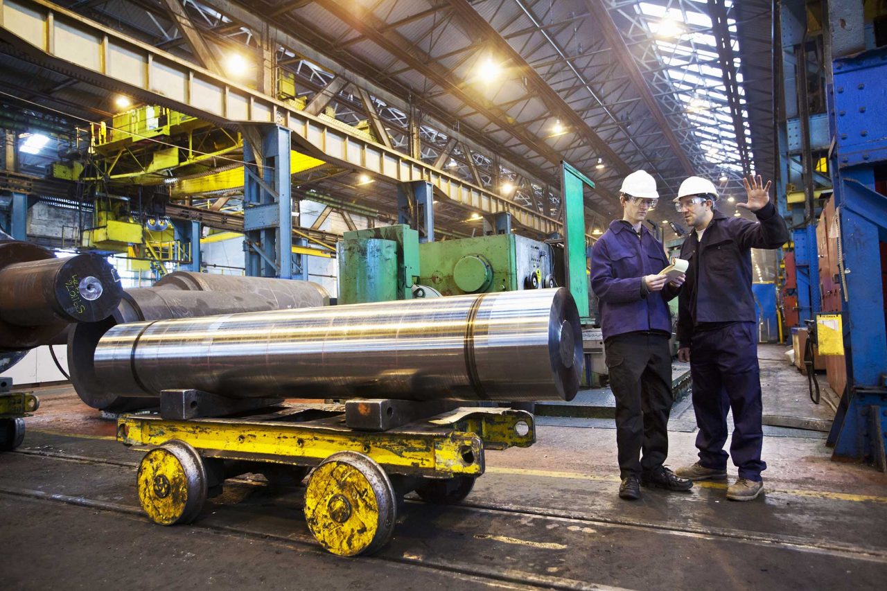 Two male workers with white hard hats talking in steel forge