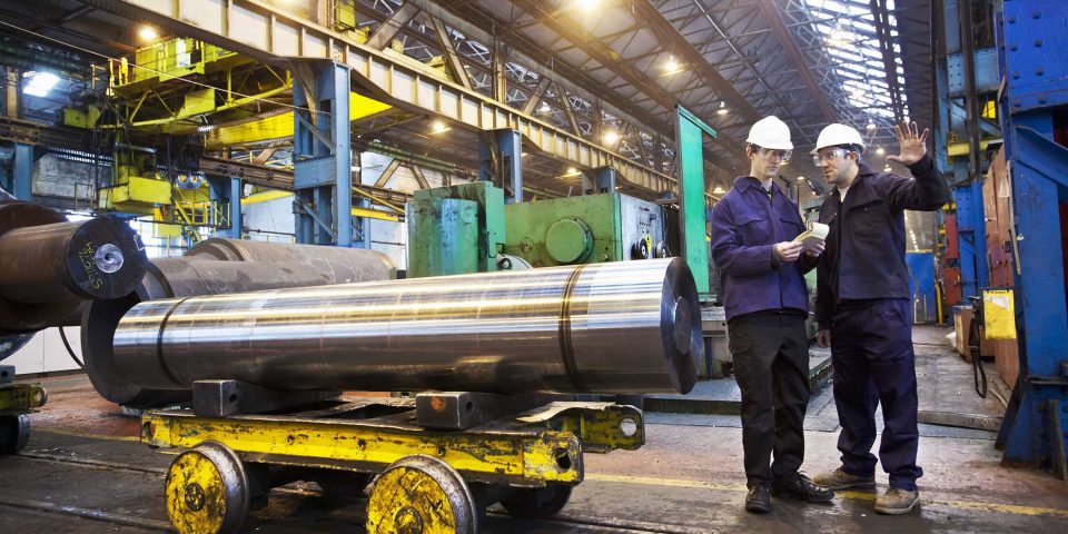 Two male workers with white hard hats talking in steel forge