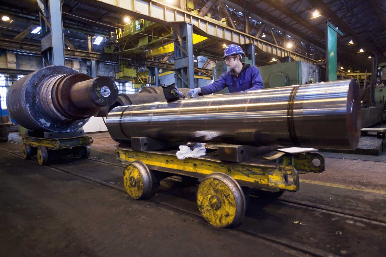 Male working in blue hard hat standing over metal steel while in a large industrial building