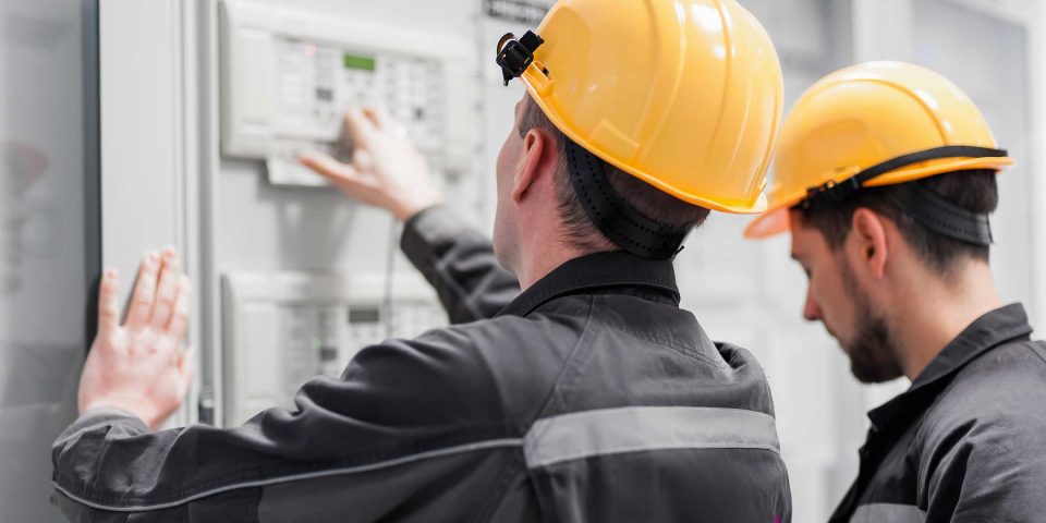 Two Field service men in yellow hard hats inspecting indoor electrical installation system