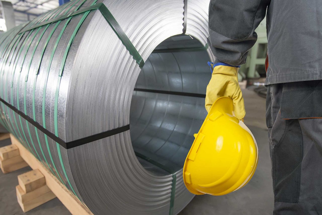 Worker with yellow protective helmet and protective gloves in front of tin metal rolls